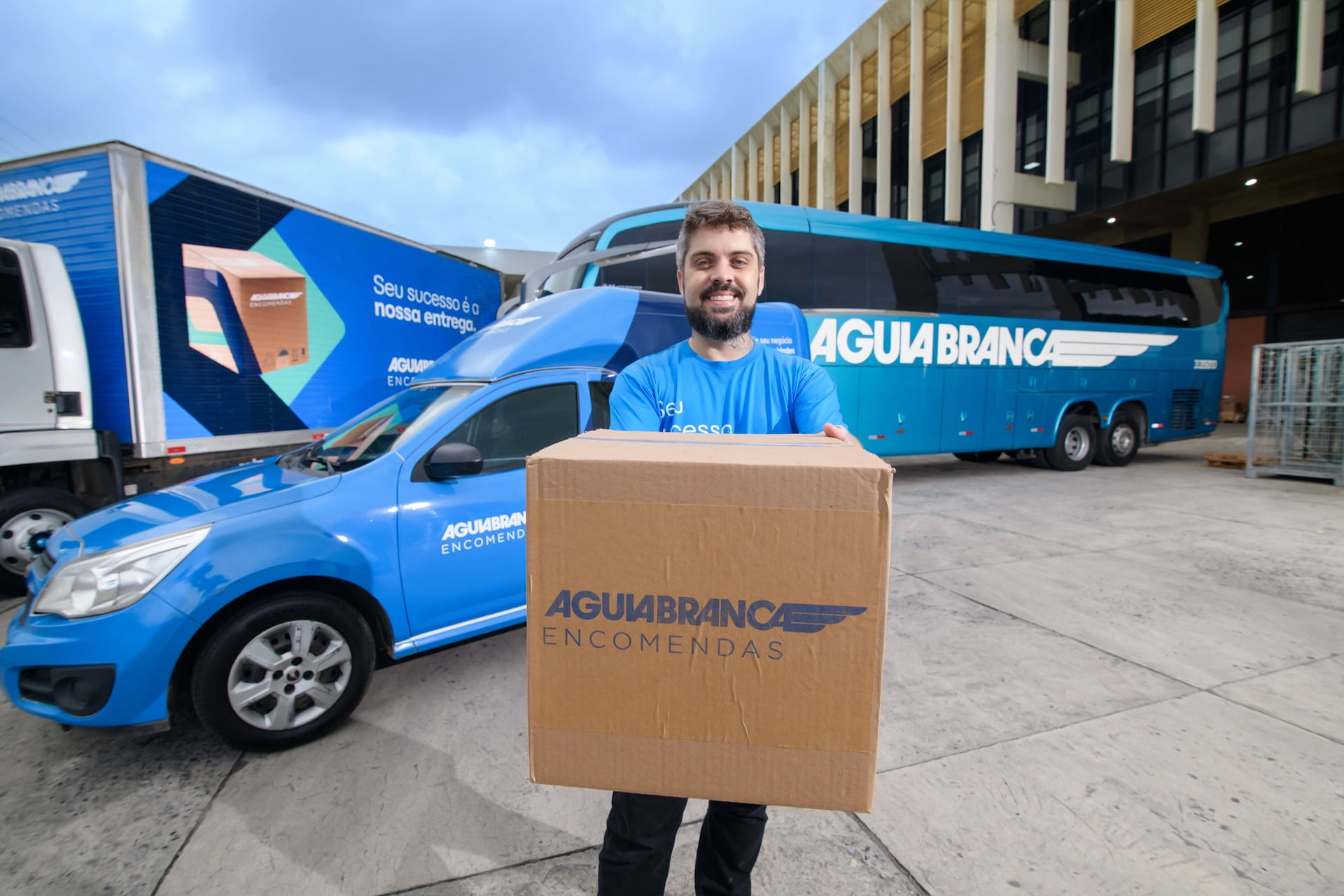 Homem carregando caixa na frente de uma van e um ônibus